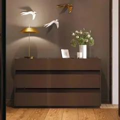 Cosa mettere sul como' della camera da letto moderna: lampada dorata, fiori in vaso bianco, cornice e candela.