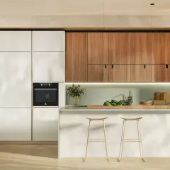 Cucina tutta altezza con ante bianche e pensili in legno. Forno integrato, isola con sgabelli dorati e dettagli verdi.