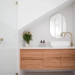 Un bagno moderno con doccia, mobile sospeso in legno, lavabo bianco e rubinetteria oro. Idee per come arredare un bagno con stile.