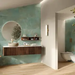 Elegante bagno verde petrolio e legno con lavabo in pietra, specchio rotondo e sanitari sospesi.