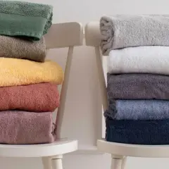 Ecco come piegare gli asciugamani in modo elegante: pile di asciugamani colorati e neutri disposti su sedie bianche.