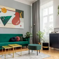 Soggiorno moderno con divano verde smeraldo, tavolini dorati e un quadro astratto. Un esempio di come abbinare i colori con stile.