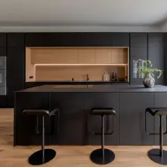 Moderna cucina nera con isola centrale e sgabelli. Un'elegante nicchia in legno chiaro illumina lo spazio, offrendo splendide idee cucina nera e legno.