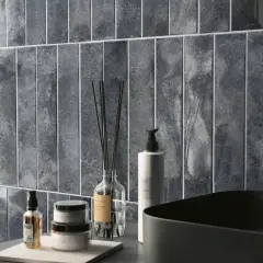 Un elegante bagno azzurro e grigio con piastrelle verticali, lavabo nero e rubinetto dorato.