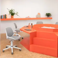 Un ufficio moderno con un tavolo arancione a forma di esagono, dotato di una vasca di palline e sedie ergonomiche.