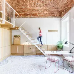 Soggiorno con soppalco a vista, soffitto in mattoni, scala bianca e una persona che sale. Arredamento moderno e minimalista.