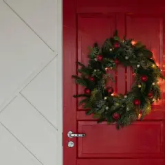 Un ingresso natalizio da sogno: una porta rossa con ghirlanda di pino, palline rosse e luci dorate per abbellire porta ingresso natale.