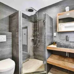 Bagno grigio chiaro e bianco con doccia in vetro, lavabo in pietra e specchio in legno.