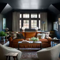 Soggiorno con divano arancione, poltrone bianche e tappeto persiano. L'arredamento boho glam è esaltato da lampade sferiche e dettagli etnici.