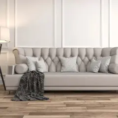 Divano imbottito beige con cuscini a righe grigie e una coperta scura. La lampada da terra nera completa l'arredamento, dimostrando che beige e grigio stanno bene insieme.