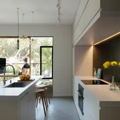 Un moderno cucina soggiorno open space di 50 mq con isola centrale, bancone con lavello e un'area cottura lineare. Una donna legge vicino alla finestra.