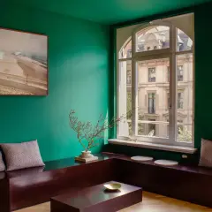 Un soggiorno moderno con pareti verde smeraldo, un quadro astratto, un divano basso in legno scuro e cuscini a quadri. I colori che stanno bene con il verde sono esaltati dal contrasto.