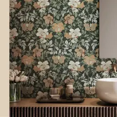 Bagno con carta da parati floreale su sfondo verde scuro, fiori bianchi e color sabbia. Lavabo bianco, specchio e rubinetteria dorata.