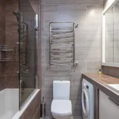 Bagno moderno con vasca, doccia, WC e una pratica lavatrice integrata sotto il lavandino.