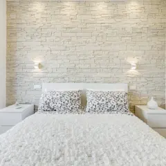 Accogliente camera da letto moderna con una suggestiva parete in pietra che fa da sfondo al letto.