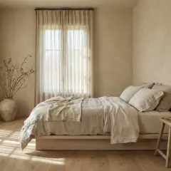 Camera da letto con pareti color sabbia e mobili chiari. Un letto con lenzuola di lino beige, un vaso con rami secchi e una candela accesa.
