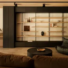 Un salotto con un divano marrone, una poltrona in pelle nera e uno scaffale aperto. Un angolo lettura con scrivania e sedia crea un piccolo giardino zen in casa.