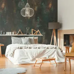 Camera da letto con carta da parati effetto materico e pittura chiara, letto bianco, camino e poltroncina gialla.