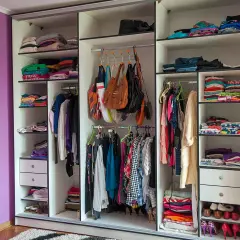 Armadio camera da letto con abiti piegati e appesi, borse e scarpe. I colori vivaci dei vestiti creano un arcobaleno.