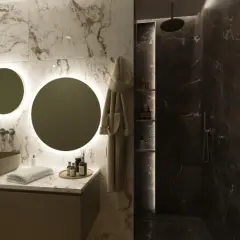 Elegante bagno scuro moderno con lavabo in pietra, specchi rotondi illuminati e doccia in marmo scuro.