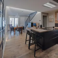 Elegante cucina soggiorno open space di 30 mq con isola nera, tavolo da pranzo in legno e scala moderna.