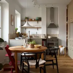 Accogliente cucina stile nordico con tavolo rotondo in legno, sedie in paglia e un grande ficus.