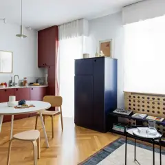 Interni di mini appartamenti con cucina rossa, tavolo rotondo, sedie in legno e un grande armadio blu.
