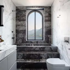 Bagno di lusso con doccia in muratura, vasca e lavabo in marmo, affacciato su un lago e montagne.