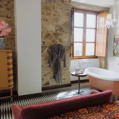 Un bagno rustico chic con vasca freestanding color pesca, pareti in pietra, un accappatoio appeso e un mobile in legno.