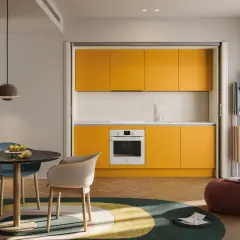 Una cucina piccola con mobili gialli vivaci, un tavolo rotondo con sedie colorate e un tappeto circolare.