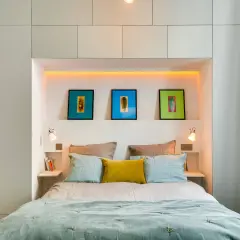 Letto moderno con nicchia illuminata, quadri colorati e comodini a scomparsa, perfetto per chi non ha spazio per i comodini.