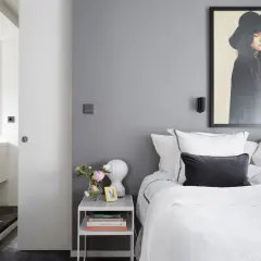 Pareti camera da letto grigia e bianche, con letto bianco, quadro di una donna con cappello e accessori appesi.