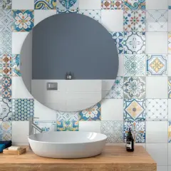 Bagno con lavabo su mobile in legno, specchio rotondo e pareti decorate con vivaci cementine bagno dai motivi geometrici e floreali.