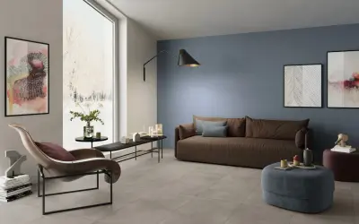 Soggiorno moderno con **pavimento grigio** e **pareti tortora** che creano un'atmosfera rilassante. Divano marrone, poltrona di design e opere d'arte completano l'arredo.