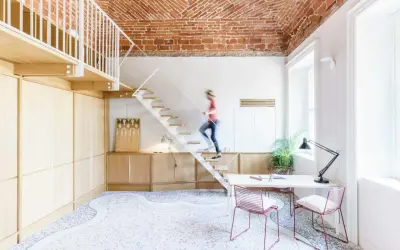 Soggiorno con soppalco a vista, soffitto in mattoni, scala bianca e una persona che sale. Arredamento moderno e minimalista.