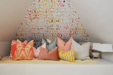 Un letto accogliente con tanti cuscini decorativi dai motivi vivaci e colorati, pronti per un riposo da sogno.