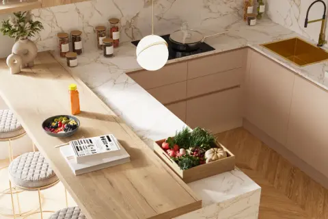 Top cucina con materiali innovativi: piano in legno chiaro, marmo bianco e oro, mobili color pesca. Frutta fresca, verdure e libri sul bancone.