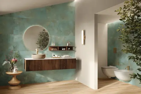 Elegante bagno verde petrolio e legno con lavabo in pietra, specchio rotondo e sanitari sospesi.