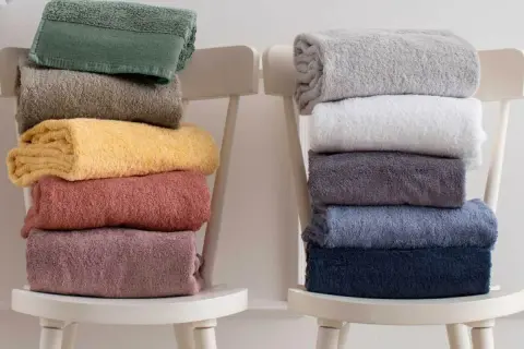 Ecco come piegare gli asciugamani in modo elegante: pile di asciugamani colorati e neutri disposti su sedie bianche.
