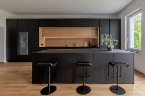 Moderna cucina nera con isola centrale e sgabelli. Un'elegante nicchia in legno chiaro illumina lo spazio, offrendo splendide idee cucina nera e legno.