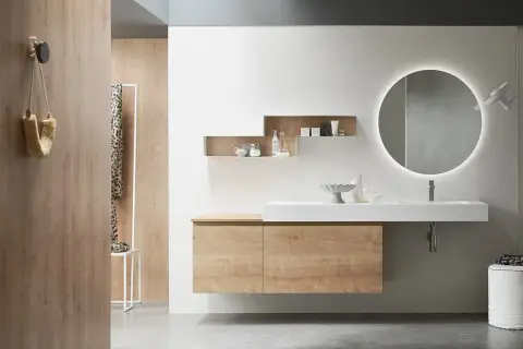 Bagno effetto legno e bianco: mobile sospeso, lavabo bianco, specchio rotondo illuminato e pareti in legno creano un ambiente moderno e accogliente.