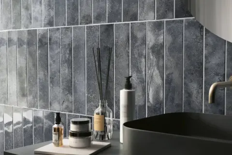 Un elegante bagno azzurro e grigio con piastrelle verticali, lavabo nero e rubinetto dorato.