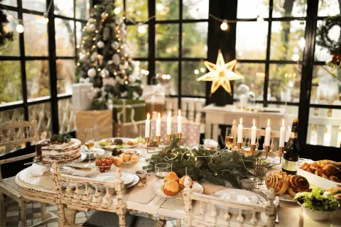 Tavola imbandita per Natale con torta, arrosti e candele. Un albero addobbato e regali creano l'atmosfera perfetta per le idee decorare la cucina per natale.