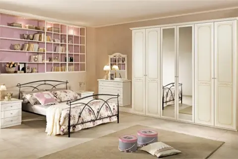 Camera da letto classica: letto in ferro battuto, armadio bianco con specchi, cassettiera e libreria a muro.