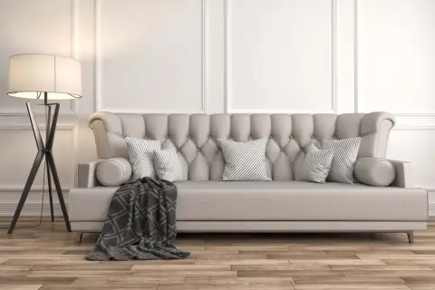 Divano imbottito beige con cuscini a righe grigie e una coperta scura. La lampada da terra nera completa l'arredamento, dimostrando che beige e grigio stanno bene insieme.