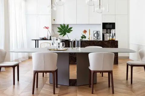 Un elegante tavolo da pranzo con sedie imbottite, parte di un progetto di casa in stile contemporaneo. La cucina moderna è visibile sullo sfondo.