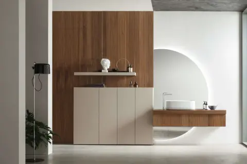 Un elegante bagno minimal con mobile sospeso in legno, lavabo bianco e specchio circolare retroilluminato.