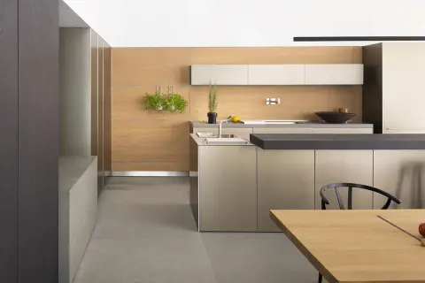 Cucina moderna con ante color tortora e pareti in legno chiaro. Un'isola centrale con piano scuro e un tavolo in legno completano l'ambiente.