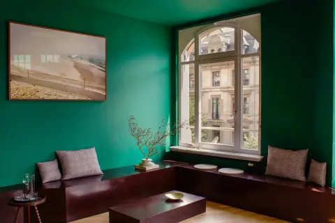 Un soggiorno moderno con pareti verde smeraldo, un quadro astratto, un divano basso in legno scuro e cuscini a quadri. I colori che stanno bene con il verde sono esaltati dal contrasto.