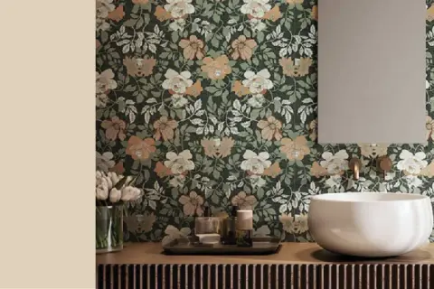 Bagno con carta da parati floreale su sfondo verde scuro, fiori bianchi e color sabbia. Lavabo bianco, specchio e rubinetteria dorata.